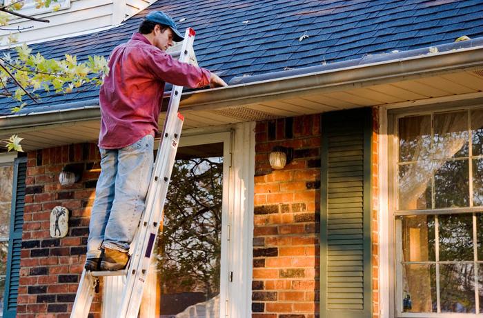 homeowner on ladder cleaning gutters and roof in grand rapids michigan